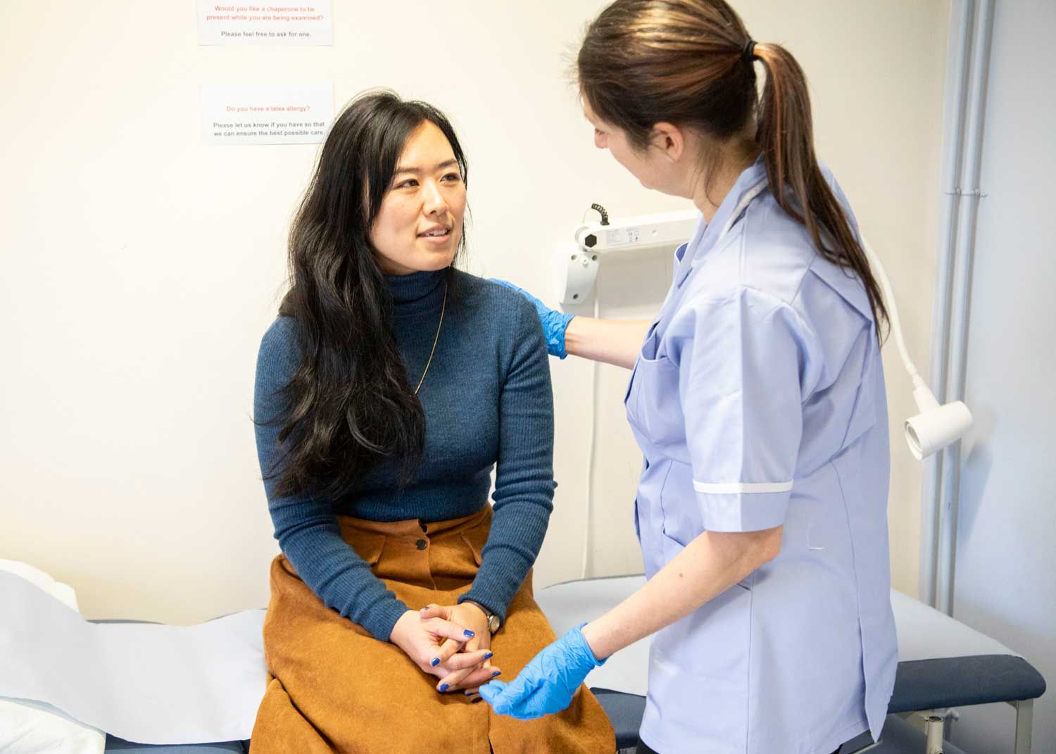 A woman sits on an exam table and talks to a nurse