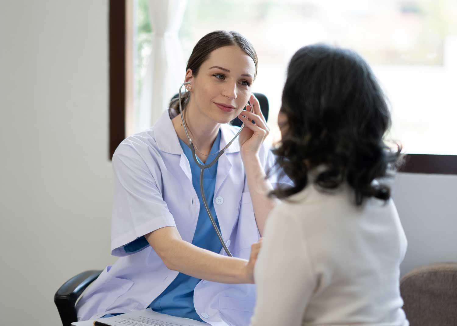 A woman sits on an exam table and talks to a nurse